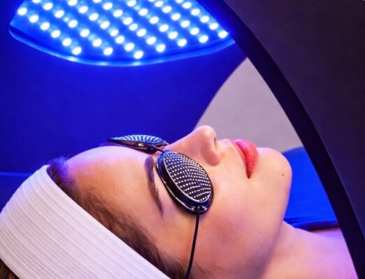 Glamcor-11 Client receiving Glamcor Time Warp LED light therapy facial at Vibrant Med Spa of NWA in Bentonville AR, with blue LED light panel for skin rejuvenation and acne treatment.